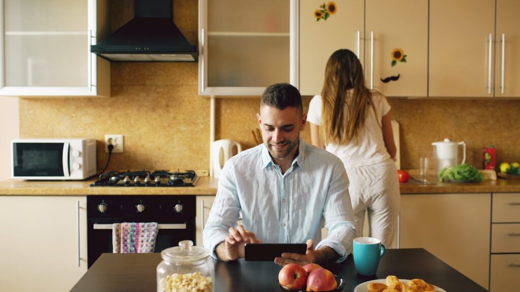 Couple sits at a bright, modern kitchen island, seriously reviewing documents and financial papers related to selling thei...