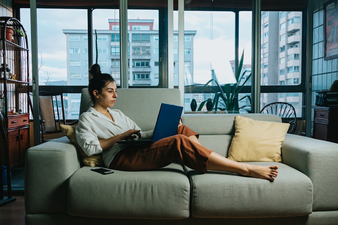 A homeowner sits in their bright and modern living room, using a laptop to research local market conditions and home pricing strategies.