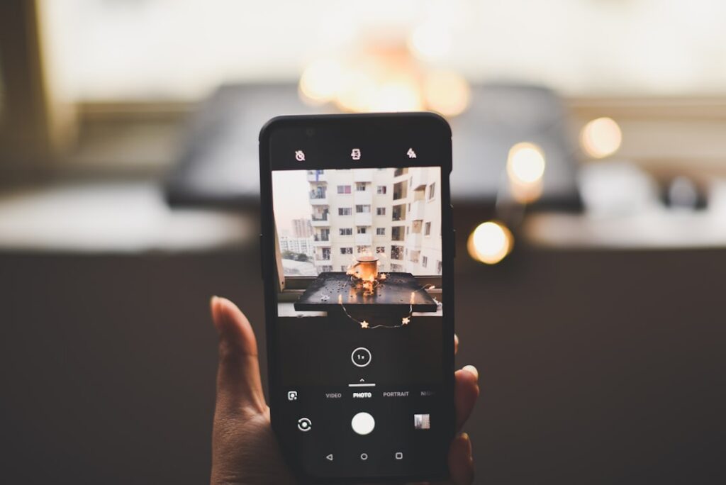 Person stands outside a modern suburban home, looking at a smartphone, representing a homeowner checking their online prop...