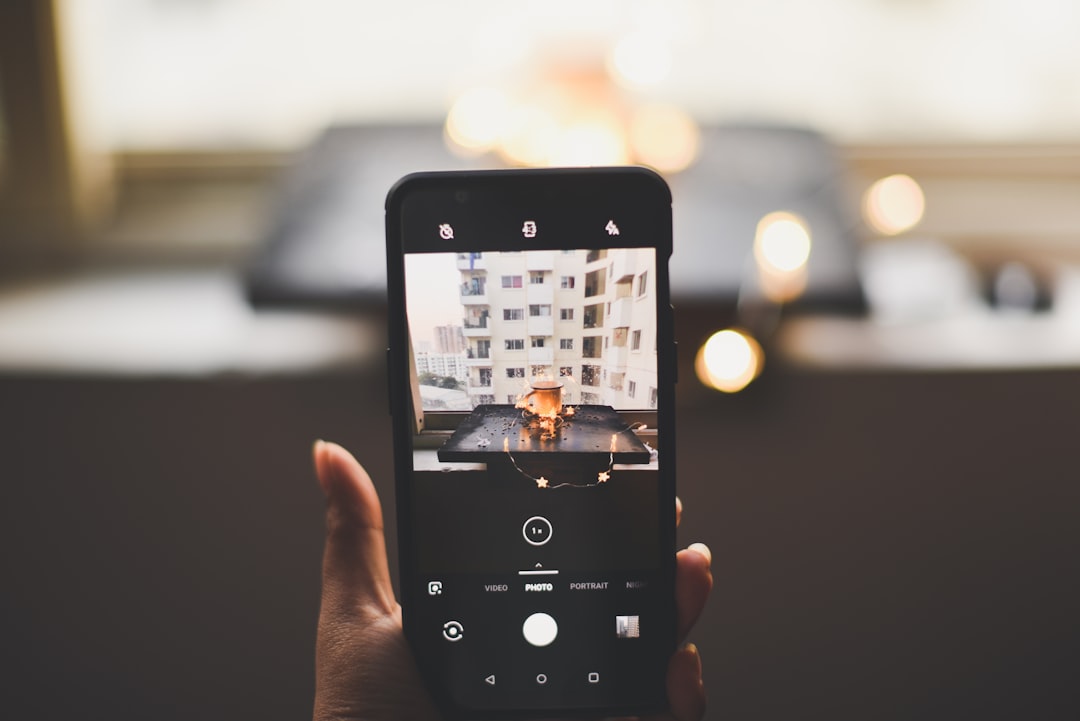 Person stands outside a modern suburban home, looking at a smartphone, representing a homeowner checking their online prop...