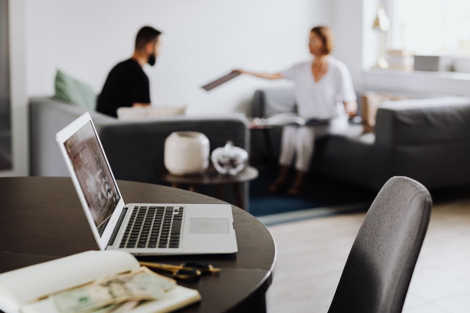 A laptop sits open on a coffee table in a bright, stylish living room, representing technology's central role in the modern real estate transaction.