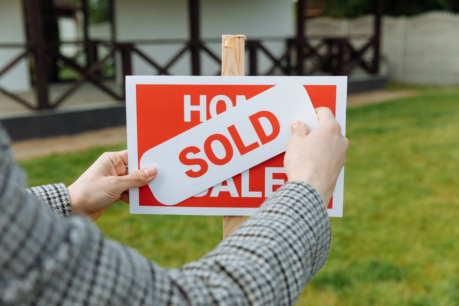 A real estate 'For Sale' sign staked in the green front yard of a welcoming single-family home in Columbus, Indiana.
