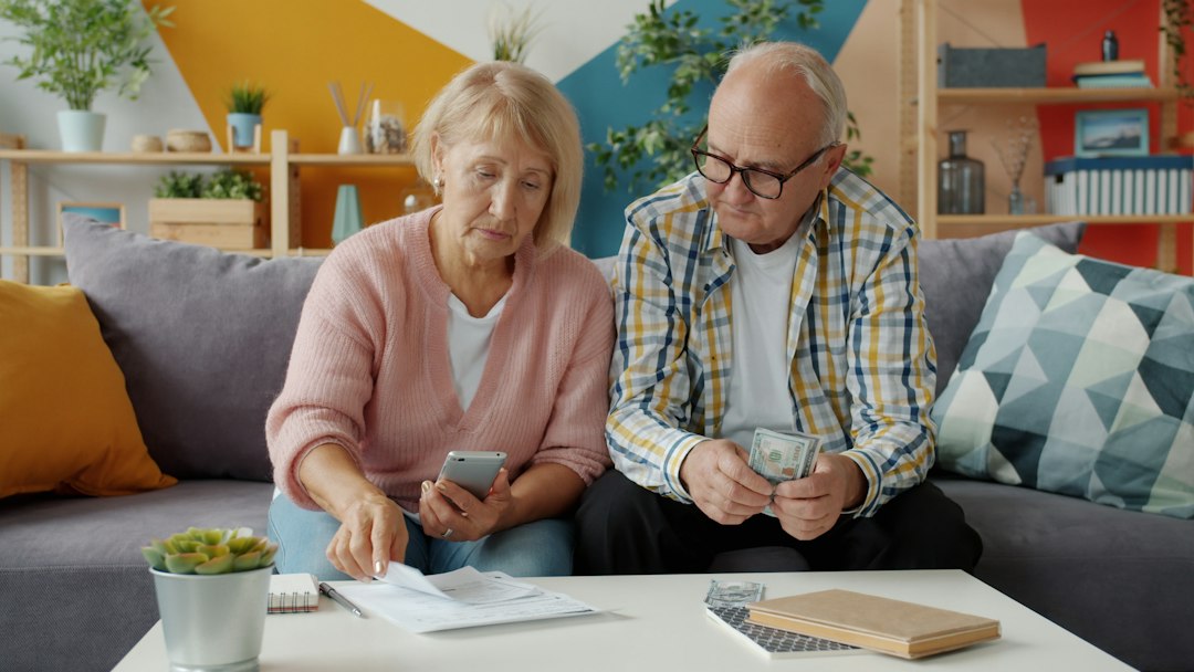Thoughtful couple sits at their kitchen table with a laptop and papers, looking concerned as they review their home financ...