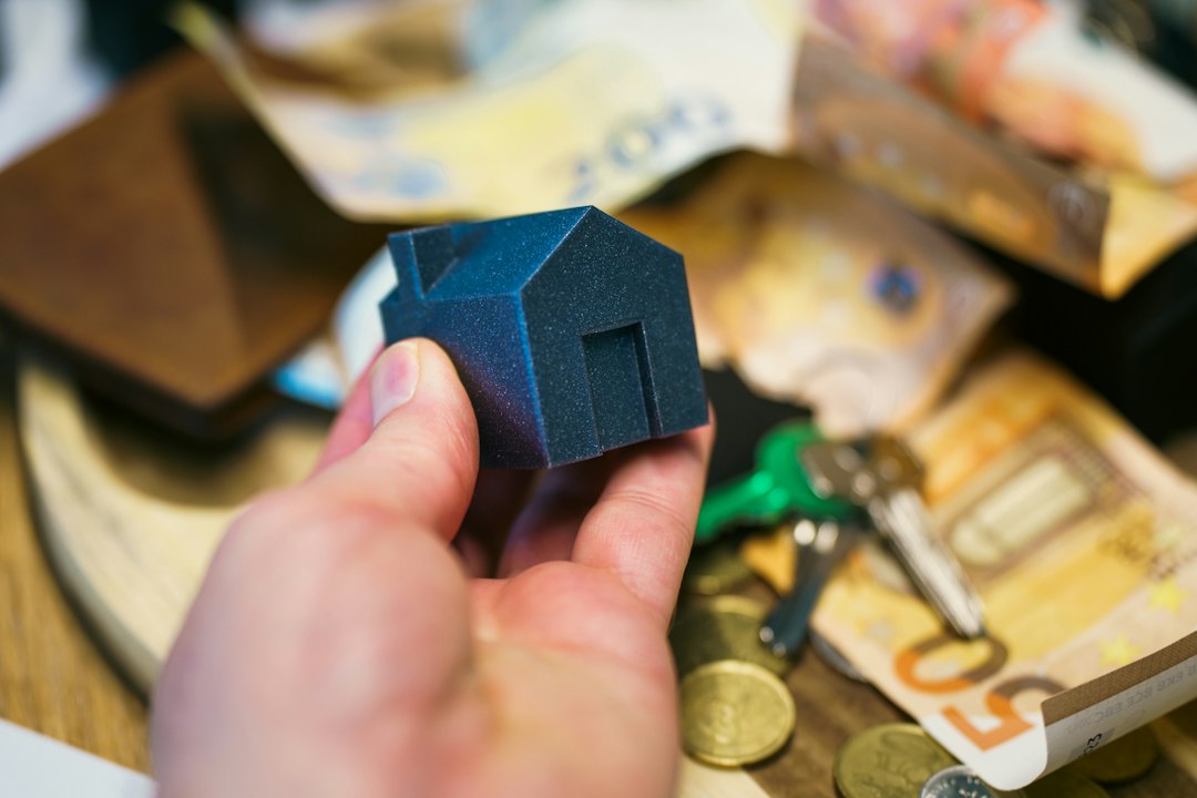 A close-up shot of a hand placing a coin into a white, house-shaped piggy bank, symbolizing the thousands of dollars in equity saved with a 1% listing.