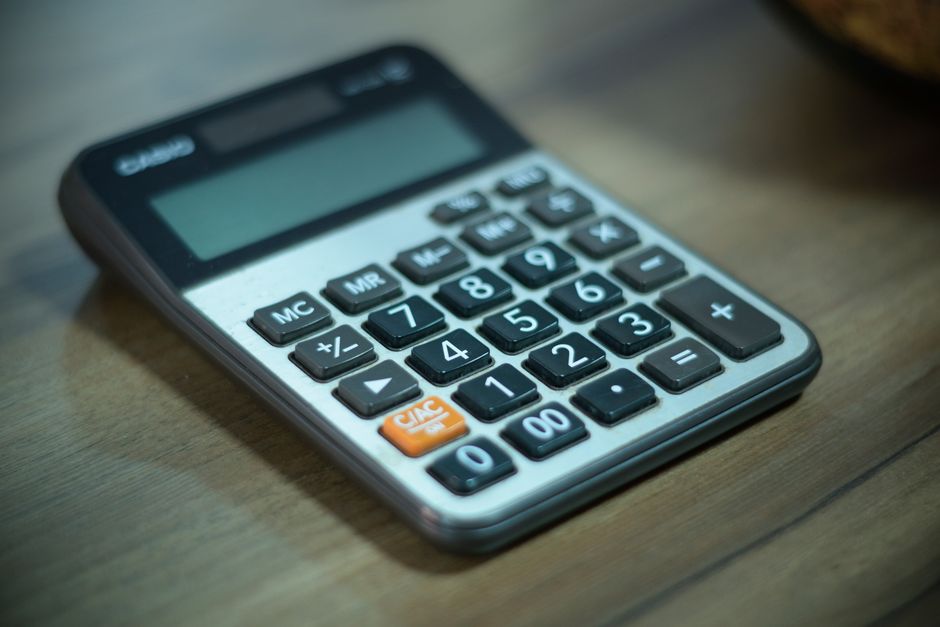 A close-up shot of modern house keys and a calculator resting on a wooden desk, symbolizing the financial calculations and costs associated with a home sale.
