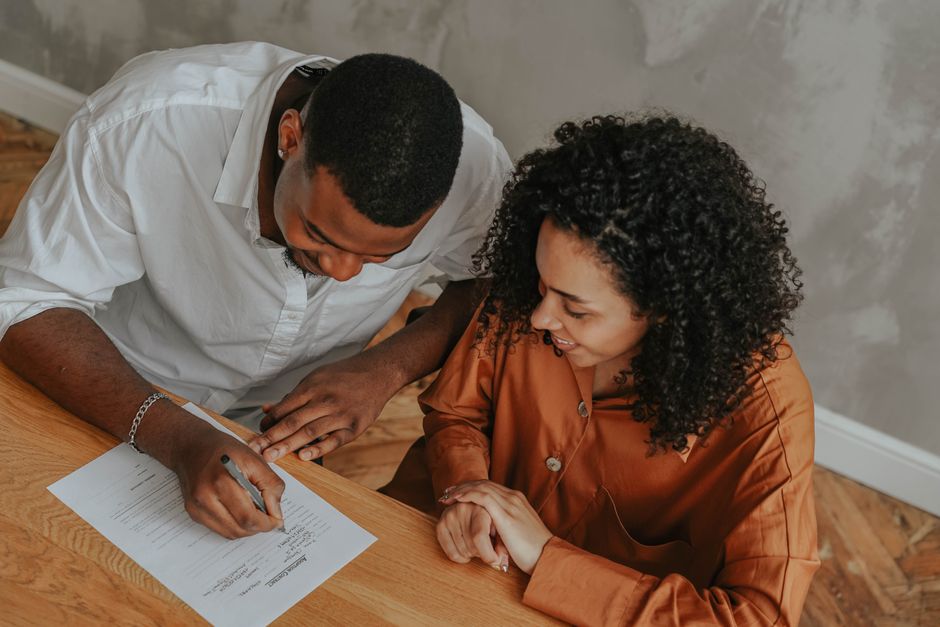 A smiling couple signs real estate documents at the island in their bright, modern kitchen, signifying a successful and financially savvy home sale.